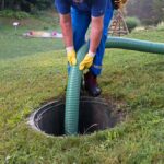 A person holding a hose is servicing a septic tank.