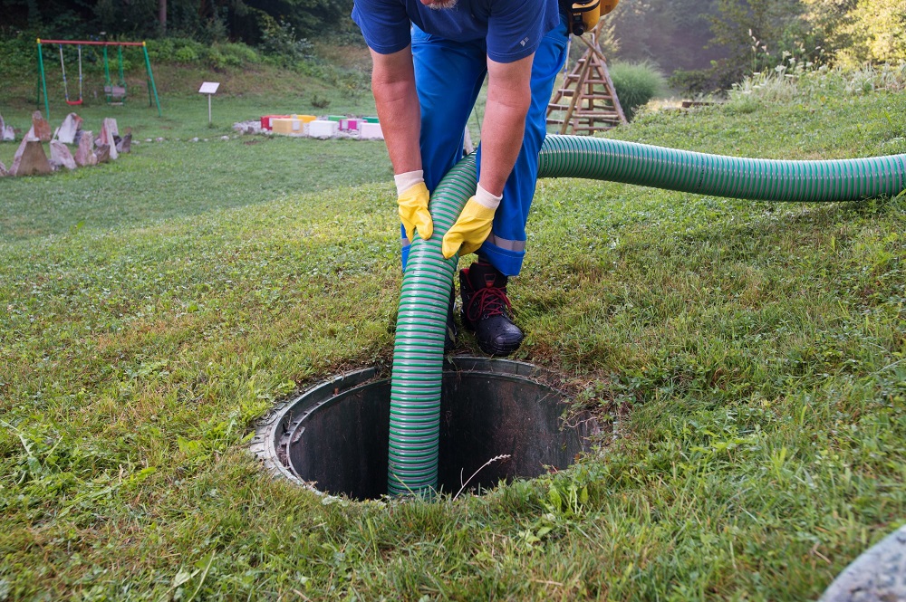 A person holding a hose is servicing a septic tank.