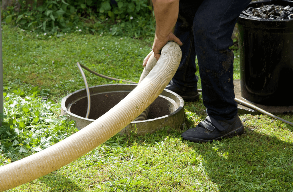 A man using a hose to drain a septic tank