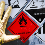 A hand in a glove placed against a barrel which features hazardous waste stickers