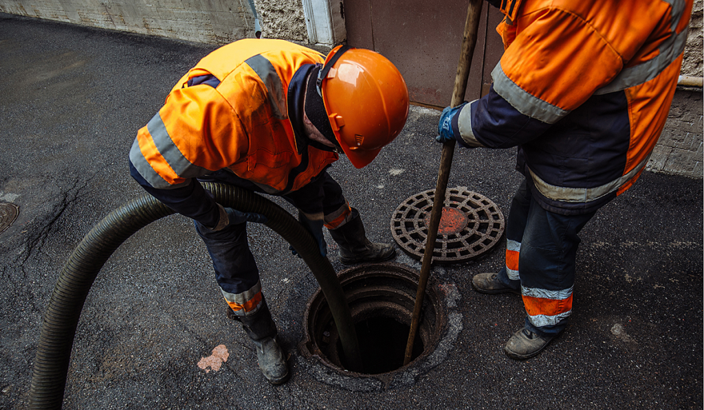 Two workers in high vis clothing placing two hoses down a manhole