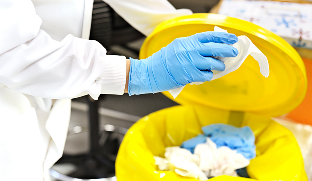 A person holding chemical waste over an open bin