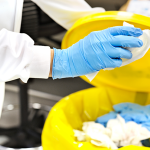 A person holding chemical waste over an open bin