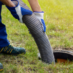 A person holding a hose placed inside a septic system in the ground