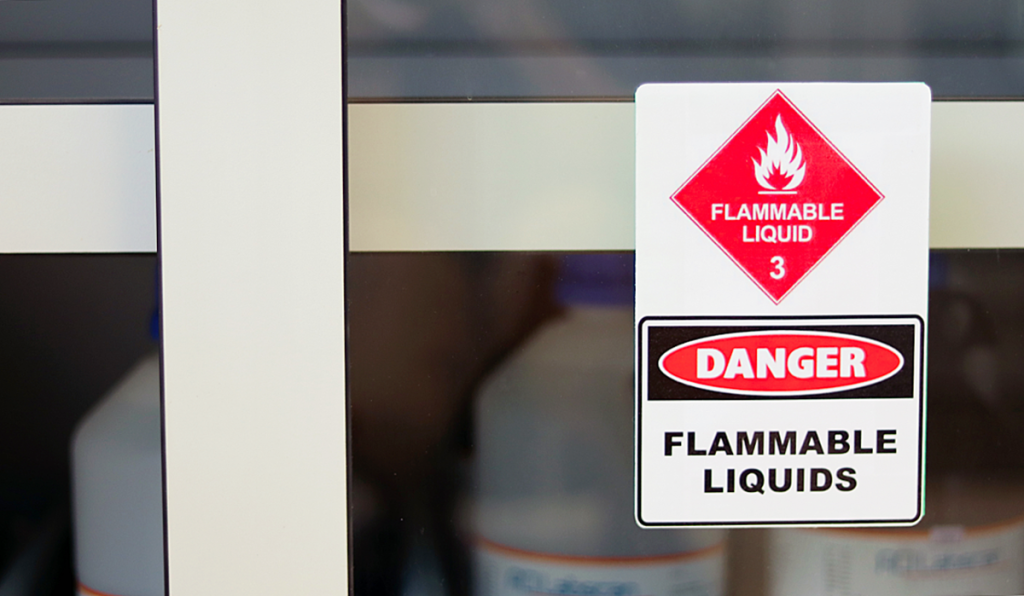 A flammable liquids warning sign placed on a shelf in front of some plastic containers
