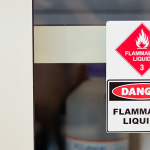 A flammable liquids warning sign placed on a shelf in front of some plastic containers