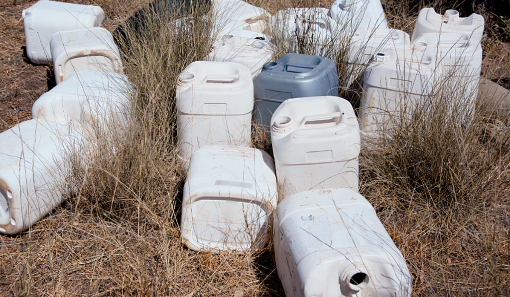 Discarded chemical containers and plastic drums stored outdoors, highlighting the need for safe chemical waste handling and disposal.