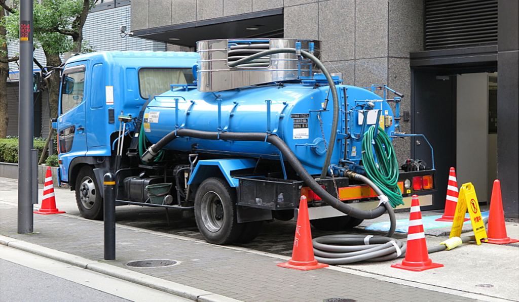 Vacuum tanker truck performing liquid waste removal outside a commercial building.