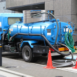 Vacuum tanker truck performing liquid waste removal outside a commercial building.