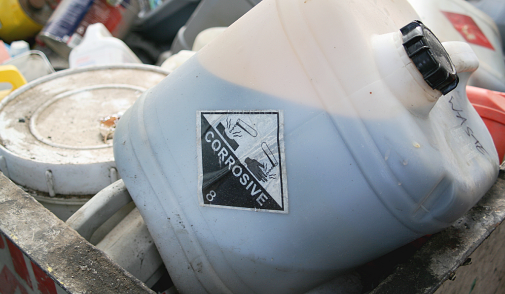 Waste oil collection container with corrosive hazard label awaiting safe disposal.