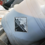 Waste oil collection container with corrosive hazard label awaiting safe disposal.