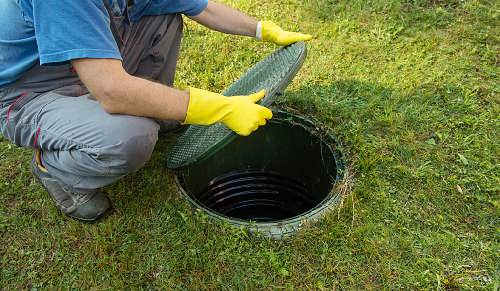 Technician opening a residential septic tank inspection cover for maintenance.