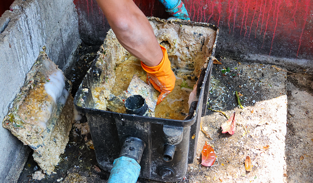 Person cleaning a commercial grease trap containing grease and food waste