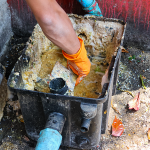 Person cleaning a commercial grease trap containing grease and food waste