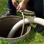 Technician pumping a septic tank using a vacuum hose