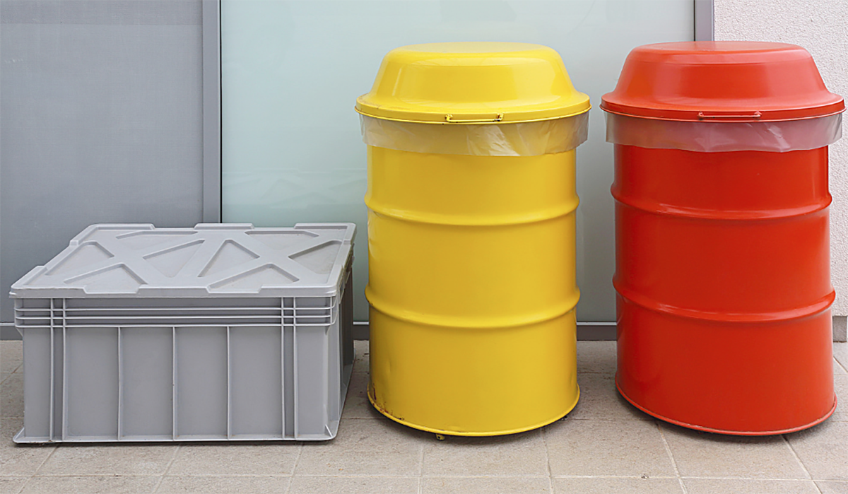 Yellow and red chemical waste drums and a grey storage container arranged in an industrial setting for chemical waste collection and storage.