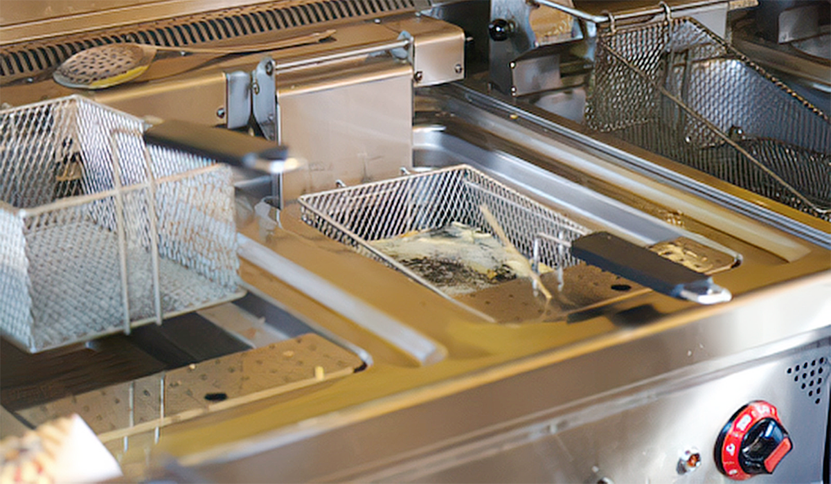 Commercial deep fryer with cooking oil and removable fryer baskets in a commercial kitchen.