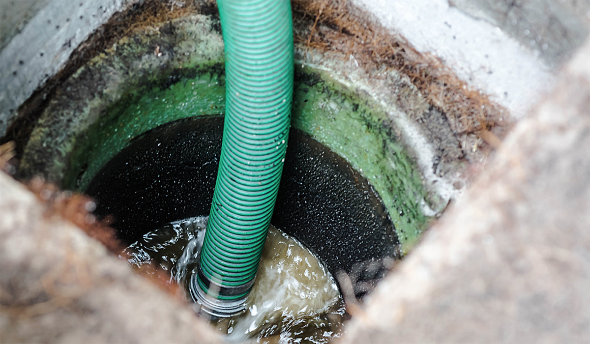 Green suction hose removing wastewater from a commercial septic tank during professional septic tank pumping and maintenance.